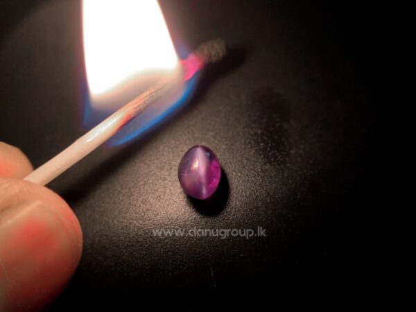 Alexandrite Cat’s Eye gemstone beside flame showing chatoyancy and red color-change response on dark background.